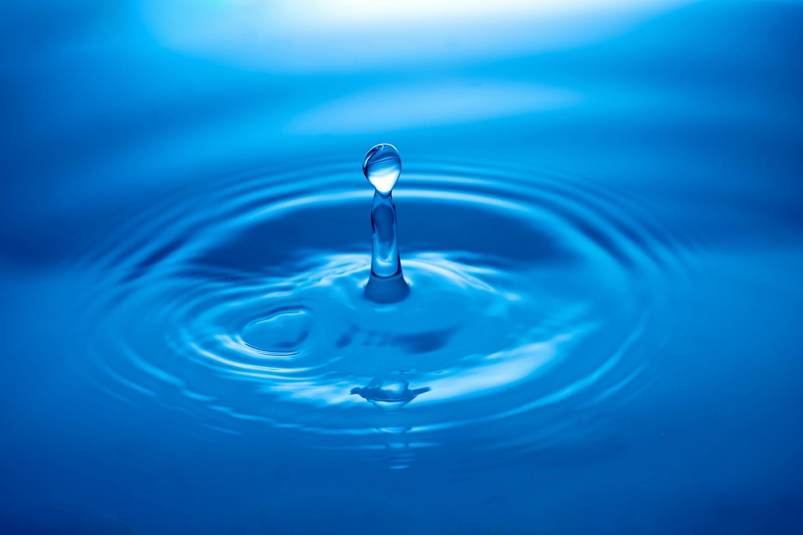 Capture of a water droplet creating ripples on a blue surface showcasing tranquility and clarity.